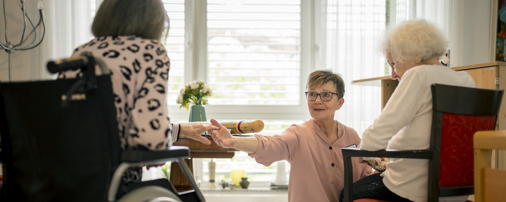 Eine Mitarbeiterin unterhält sich mit zwei Bewohnerinnen und reicht einer der beiden die Hand.