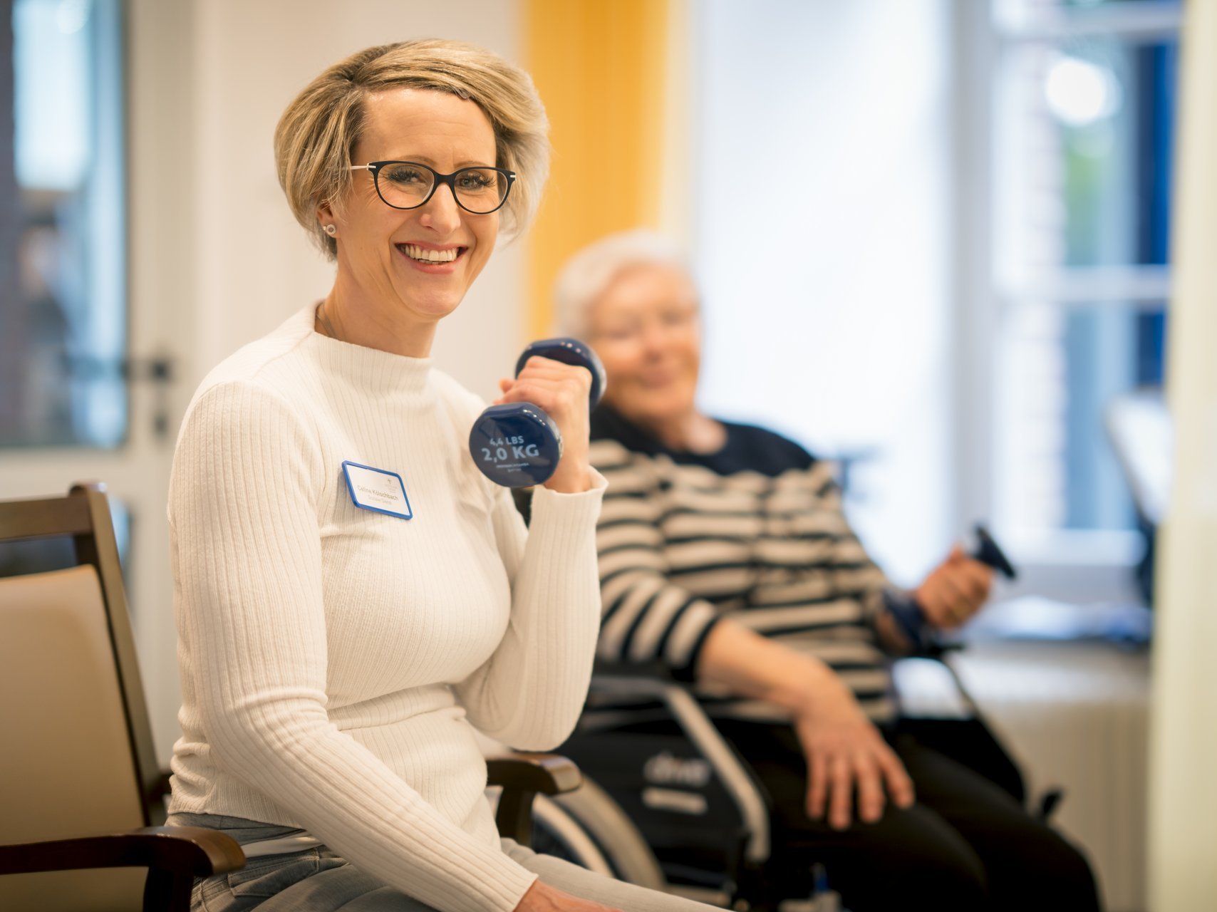 Eine Gruppe von Bewohnenden trainiert gemeinsam mit einer Mitarbeiterin mit kleinen Hanteln.