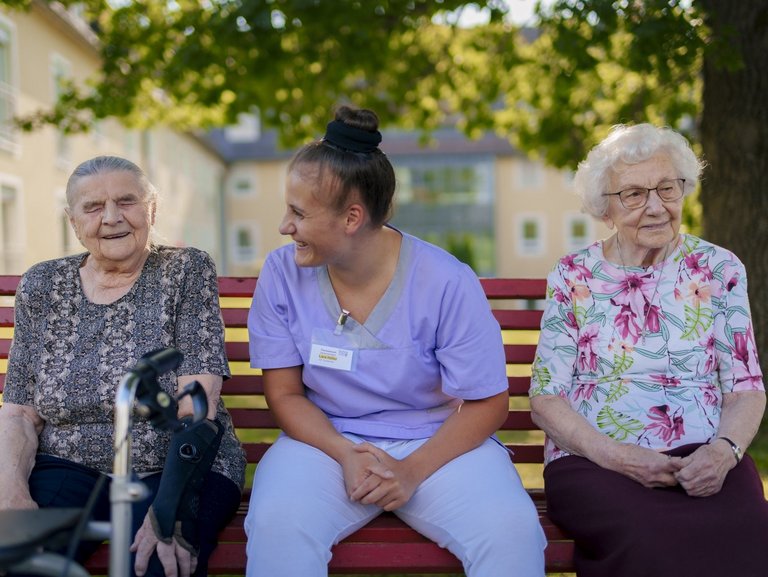 Eine Pflegerin unterstützt Bewohner/innen beim Kartenspiel auf der Terasse